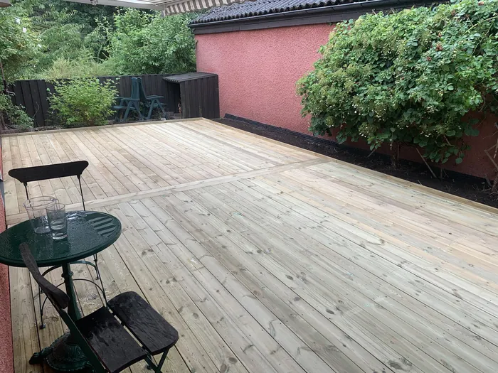 Terrasse avec table basse, près d'une maison rouge et d'une haie